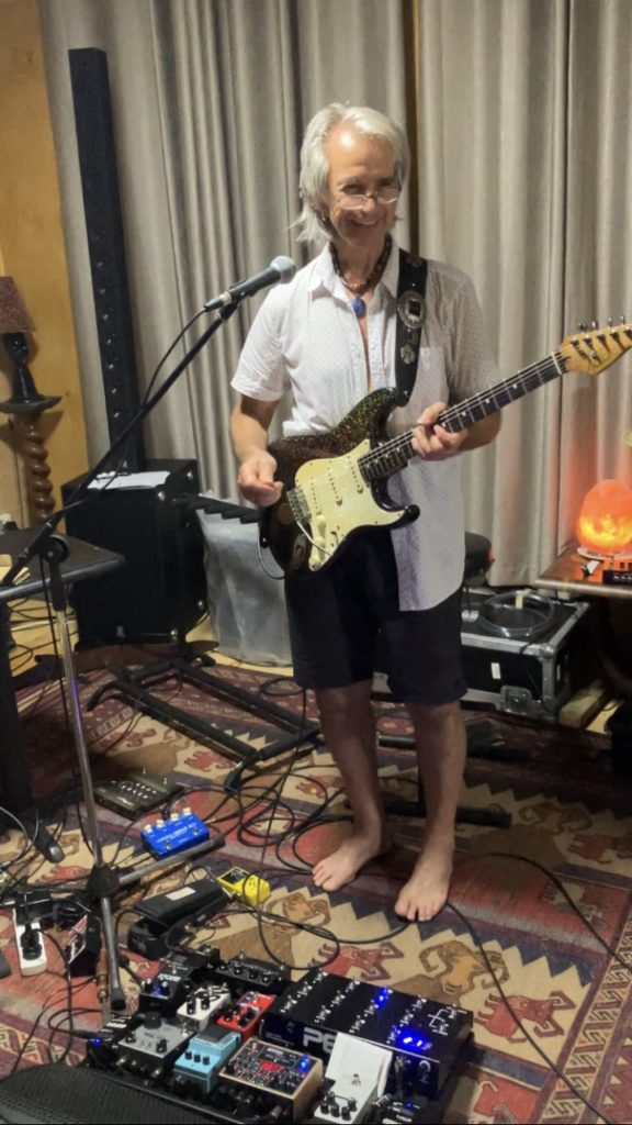 Foto usmievajúceho sa Kevina Boricha s gitarou v štúdiu.